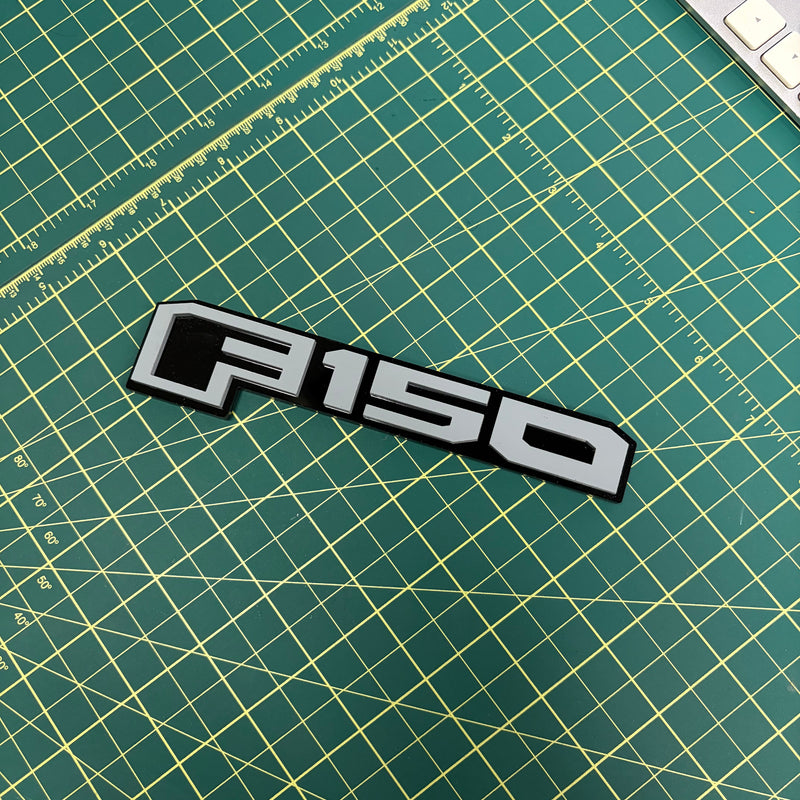 Load image into Gallery viewer, Light gray ford F150 emblem on a green mat
