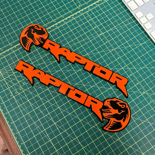 Pair of orange raptor emblems with dinosaur heads on a green mat